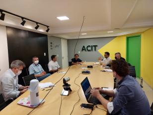 Reunião de diretores da Fomento Paraná e SGC central na Associação Comercial e Empresarial de Toledo. Diretores das duas entidades sentados ao redor de uma mesa, assistem transmissão online.
