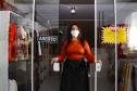 A empresária Josiane Duarte, proprietária de uma loja de roupas para o público evangélico, em Piraquara. Na foto ela está na porta da loja, em vidro, com placa de "aberto", e dá para ver as roupas atrás dela.