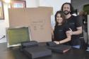 Patrícia Motta e Daniel Cortezia são jovens, brancos, de cabelos escuros, ele é mais alto e usa barba e cabelos compridos. Eles vestem camisetas pretas e mostram produtos da cartonagem que montaram com recursos da Fomento Paraná