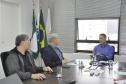Claudio Stabile, de camisa azul claro, à direita, conversa com Jorge Callado e Julio Suzuki, todos sentados. Há uma janela aberta atrás do Claudio, sobre a mesa à copos de água e alguns papéis.