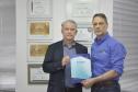 Dois homens brancos, Claudio Stabile, de camisa azul claro, à direita, e Jorge Callado, posam apresentando uma pasta de papel com uma iscrição na capa com o nome IPARDES, presidido por Callado.