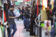 Corredor de uma loja de roupas, com diversas camisetas coloridas e homens e mulheres olhando as roupas