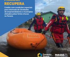 Bombeiros passam por área alagada carregando bote inflável na cor laranja. Um quadro na cor azul com texto em branco informa sobre linhas de crédito em condições especiais par aempreendedores de municípios afetados pela chuva.