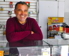 Na imagem, vemos o empreendedor Sandro Silva em sua LanHouse. Sandro é um jovem senhor branco. Na foto, ele usa uma blusa vermelha. 