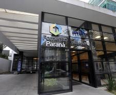 Imagem da fachada da sede da Fomento Paraná em Curitiba. É uma parede envidraçada em módulos tipo fumê com logotipos da Fomento, Invest e Governo