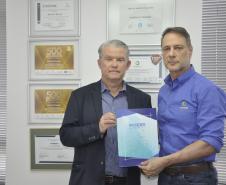 Dois homens brancos, Claudio Stabile, de camisa azul claro, à direita, e Jorge Callado, posam apresentando uma pasta de papel com uma iscrição na capa com o nome IPARDES, presidido por Callado.
