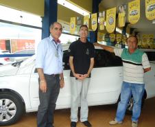 Agente de crédito Reinaldo Ribeiro acompanha os taxistas Estevan Cezar de Oliveira e Rosinei Veronez de Aguiar ao receberem as chaves dos novos veículos.