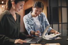 Duas mulhers conversando sobre negócios analisando contas no computador e papéis