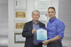 Dois homens brancos, Claudio Stabile, de camisa azul claro, à direita, e Jorge Callado, posam apresentando uma pasta de papel com uma iscrição na capa com o nome IPARDES, presidido por Callado.