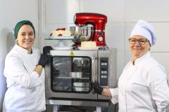 Neusa (à direita), como novo forno e batedeira da empresa familiar adquiridos com financiamento da Fomento Paraná por intermédio da Prefeitura de Curitiba.