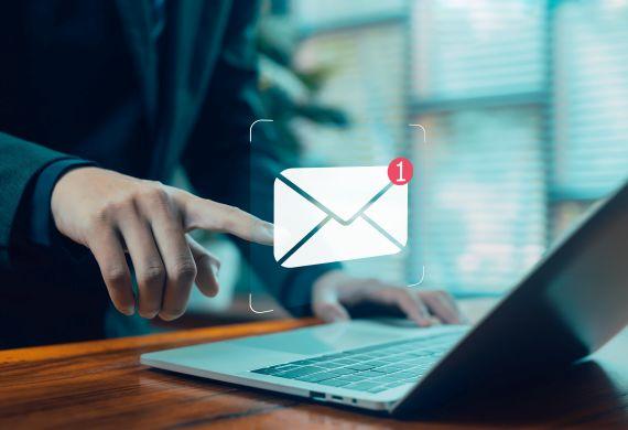 Solicite um contato. A imagem mostra parte do corpo de uma pessoa que aponta o dedo indicador para uma um ícone de envelope, símbolo de e-mail, sobre um laptop. Com uso de IA. 