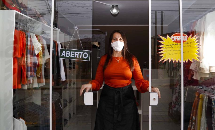 A empresária Josiane Duarte, proprietária de uma loja de roupas para o público evangélico, em Piraquara. Na foto ela está na porta da loja, em vidro, com placa de "aberto", e dá para ver as roupas atrás dela.