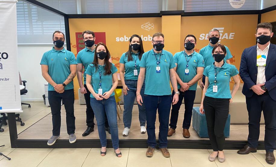 Equipe da diretoria de Mercado performada em pé, todos com camisetas verdes com logotipo da Fomento, durante encontro regional em Ponta Grossa.