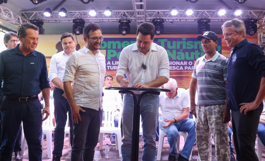 O governador Ratinho Júnior assina contrato de financiamento para o pescador Edvaldo dos Santos, acompanhado do diretor presidente da Fomento Paraná, Heraldo Neves, e outras autoridades.