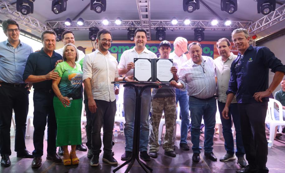 O governador Ratinho Júnior mostra contrato assinado com o pescador Edvaldo dos Santos, acompanhado do diretor presidente da Fomento Paraná, Heraldo Neves, e outras autoridades.