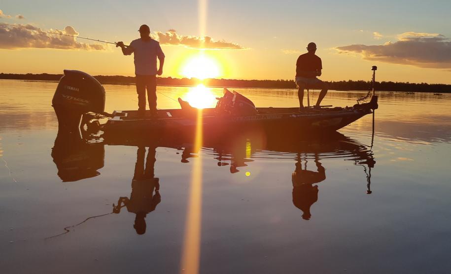Barco a motor com dois pescadores pescando no por do sol, que se reflete na água