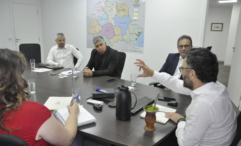 Reunião entre diretores da Fomento paraná e do BDMG em uma sala com uma grande mesa de reuniões