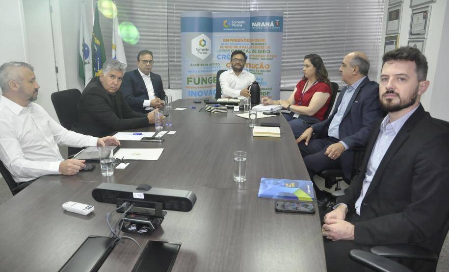 Reunião entre diretores da Fomento paraná e do BDMG em uma sala com uma grande mesa de reuniões