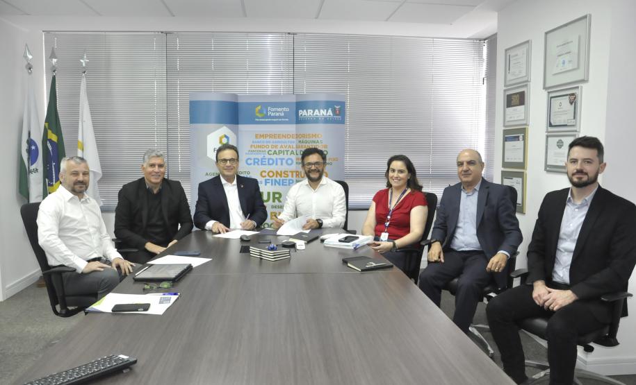 Reunião entre diretores da Fomento paraná e do BDMG em uma sala com uma grande mesa de reuniões