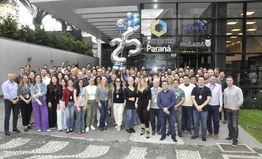 A imagem mostra grupo de mais de 100 colaboradores da Fomento Paraná posando para foto em frente à empresa