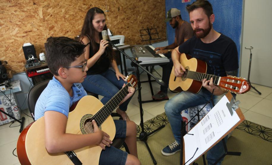 Escola de Palmeira atende estudantes de música de todas as idades. Empreendedor usou a linha da Fomento Paraná, desenvolvida em parceria com a Secretaria de Estado da Cultura para apoiar empreendimentos da economia criativa. Na imagem, os alunos Alexandre Pinheiro Neto e Paloma de Jesus Cubas com o professor Rodrigo Haniskievicz e Webis Duarte (ao fundo).