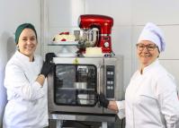 Neusa (à direita), como novo forno e batedeira da empresa familiar adquiridos com financiamento da Fomento Paraná por intermédio da Prefeitura de Curitiba.