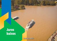 Imagem aérea de dois barcos turisticos navegando em um trecho de rio. à esqueda, sobre um fundo em grafismo verde aparede o texto juros baixos e embaixo uma legenda do audio escrito "cada vez mais"